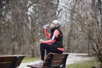 Зріла жінка тренується в парку, п'є пляшкову воду — стокове фото