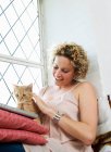 Середня доросла жінка погладжує кота і використовує ноутбук — стокове фото