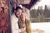Retrato de pareja de pie fuera de la cabaña de troncos en invierno, Elmau, Baviera, Alemania - foto de stock