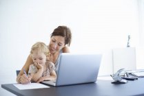 Mulher adulta média escrevendo notas com a filha criança em seu colo — Fotografia de Stock