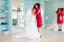 Дочка намагається на весільній сукні, обіймаючи матір — стокове фото