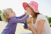 Menina colocando creme solar na mãe — Fotografia de Stock
