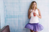 Menina de pé contra a parede azul com smoothie vermelho em suas mãos — Fotografia de Stock