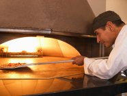 Повар пиццы кладет пиццу в духовку — стоковое фото