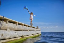 Young girl standing on wooden post on pier, holding helium balloon — Stock Photo