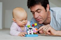 Mature man and baby daughter playing with toy cow — Stock Photo
