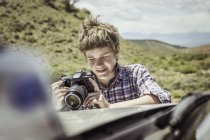 Teenage boy reviewing digital SLR on off road vehicle hood, Bridger, Montana, USA — Stock Photo