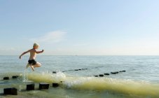Boy jumping on posts in ocean — Stock Photo
