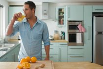 Un hombre en la cocina bebiendo jugo de naranja - foto de stock
