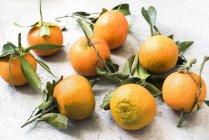 Спелые апельсины с листьями на бетонной поверхности — стоковое фото