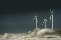Turbinas eólicas con olas de tormenta y nubes en la costa - foto de stock