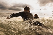 Dos amigos en el mar, remando en las tablas de surf, vista trasera - foto de stock