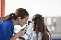 Медсестра среднего возраста, использующая отоскоп на девочке — стоковое фото