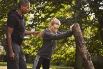 Young woman with personal trainer lifting tree trunk in park — Stock Photo