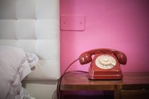 Red rotary telephone on bedside table — Stock Photo