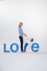 Madre e hijo tomados de la mano, de pie entre letras tridimensionales, creando la palabra AMOR - foto de stock