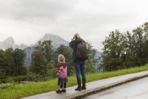 Vista trasera de los excursionistas madre e hija contemplando el paisaje desde la carretera, Berchtesgaden, Watzmann, Baviera, Alemania - foto de stock