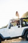 Woman sitting on roof of jeep on beach — Stock Photo
