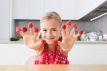 Chica poniendo frambuesas en los dedos - foto de stock