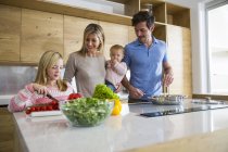 Menina e família preparando legumes frescos na cozinha — Fotografia de Stock