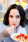 Mujer comiendo papas fritas con ketchup y mirando hacia otro lado - foto de stock