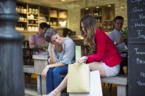 Zwei junge Freundinnen mit Einkaufstüten unterhalten sich vor einem Café — Stockfoto