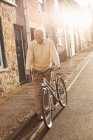 Старший чоловік штовхає велосипед на вулицю — стокове фото