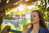 Teenager-Mädchen sitzt auf Bank und trinkt Erfrischungsgetränk aus Flasche — Stockfoto