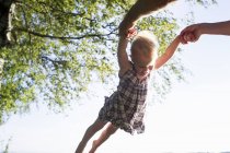 Father swinging baby girl in air, outdoors, low angle view — Stock Photo