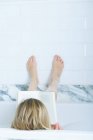 Vista posteriore della ragazza dai capelli biondi che legge un libro in bagno con i piedi in su — Foto stock