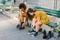 Young couple on park bench putting on rollerblades — Stock Photo