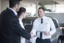 Mid adult couple making deal with salesman in car dealership — Stock Photo