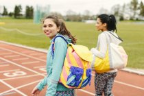Two young women walking on running track, carrying sports bags, rear view — Stock Photo