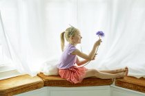 Ragazza che indossa tiara, tenendo il fiore alla finestra a baia — Foto stock