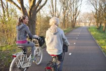 Visão traseira das mulheres pedalando na estrada arborizada — Fotografia de Stock