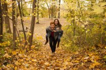 Romantic young man giving girlfriend a piggy back through autumn forest — Stock Photo