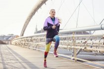 Mid adult female runner running at speed on city footbridge — Stock Photo