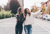 Twin sisters, walking outdoors, taking selfie using smartphone — Stock Photo