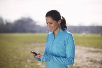 Young woman training, selecting smartphone music on playing field — Stock Photo