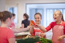 Teenage girls holding up chilies and carrots in kitchen — Stock Photo