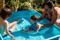 Mãe e filhos que jogam na piscina inflável no dia de verão — Fotografia de Stock