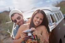 Mujer joven sosteniendo la cámara con el novio en el viaje por carretera, sonriendo - foto de stock