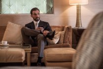 Молодий бізнесмен сидить на готельному лобі дивані за допомогою смартфона — стокове фото