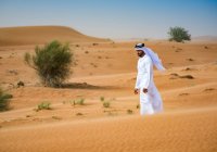 Homem do Oriente Médio vestindo roupas tradicionais andando no deserto, Dubai, Emirados Árabes Unidos — Fotografia de Stock