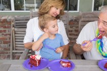 Nieto y madre viendo hombre mayor comer pastel de cumpleaños - foto de stock
