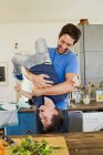 Pai segurando pequeno filho de cabeça para baixo na cozinha — Fotografia de Stock