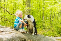 Мальчик сидит с собакой в лесу — стоковое фото