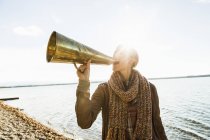 Young woman using megaphone by lake — Stock Photo