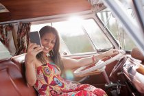 Молода жінка, використовуючи мобільний телефон у фургоні, посміхається — стокове фото