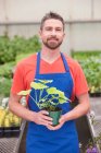 Homme adulte moyen tenant une plante dans une jardinerie, portrait — Photo de stock